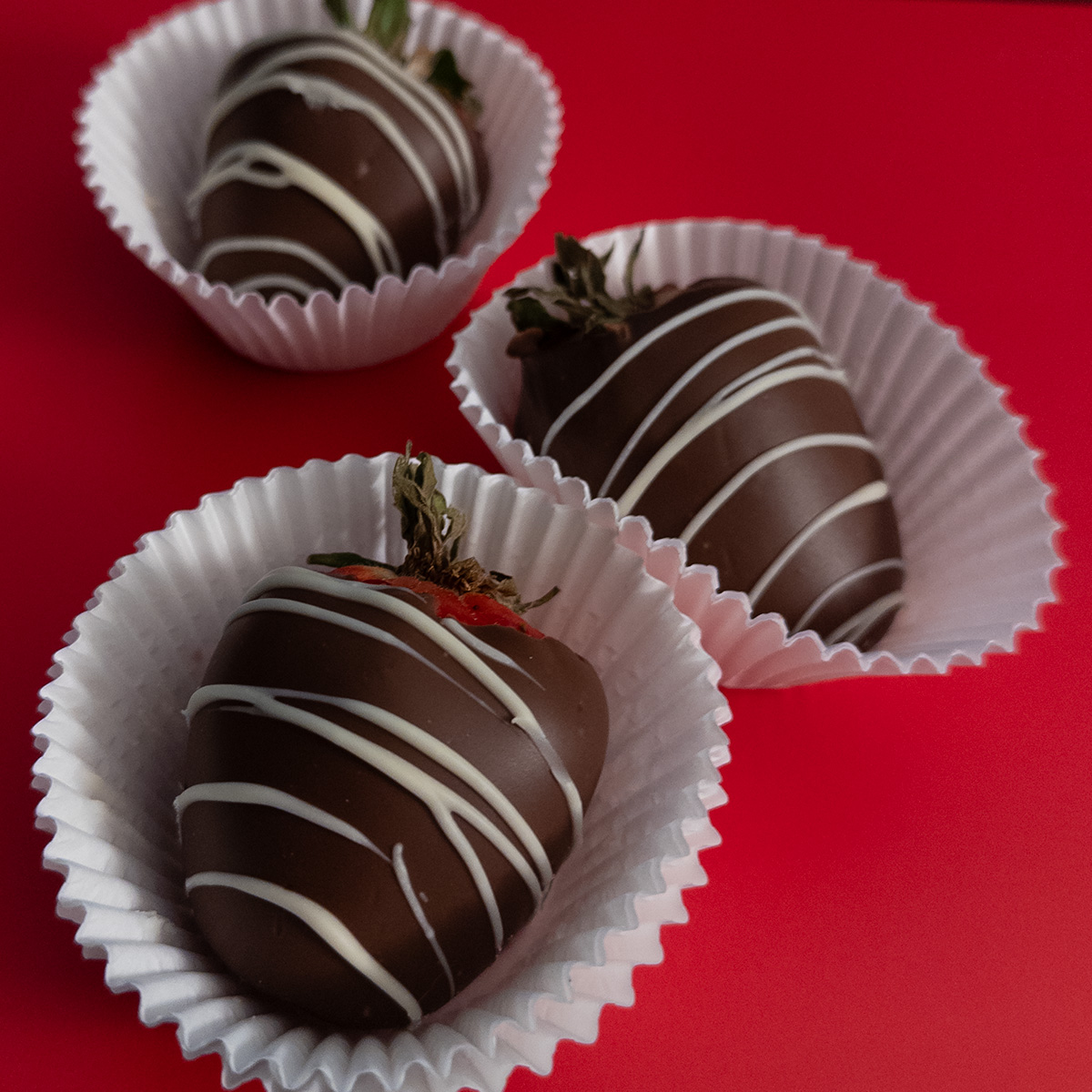 Three chocolate strawberries on a bright red background.