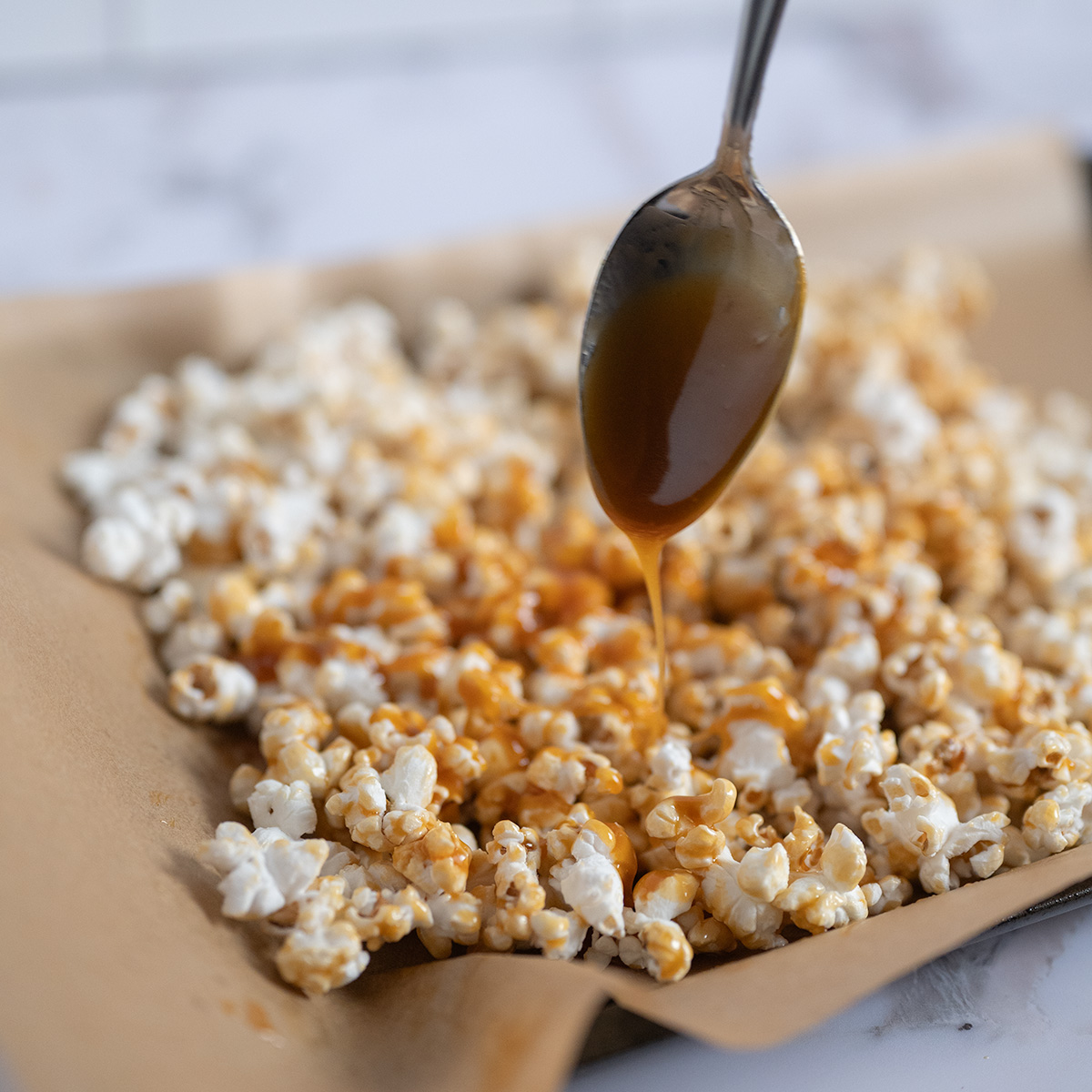 Caramel drizzling off of a spoon onto freshly-popped popcorn.