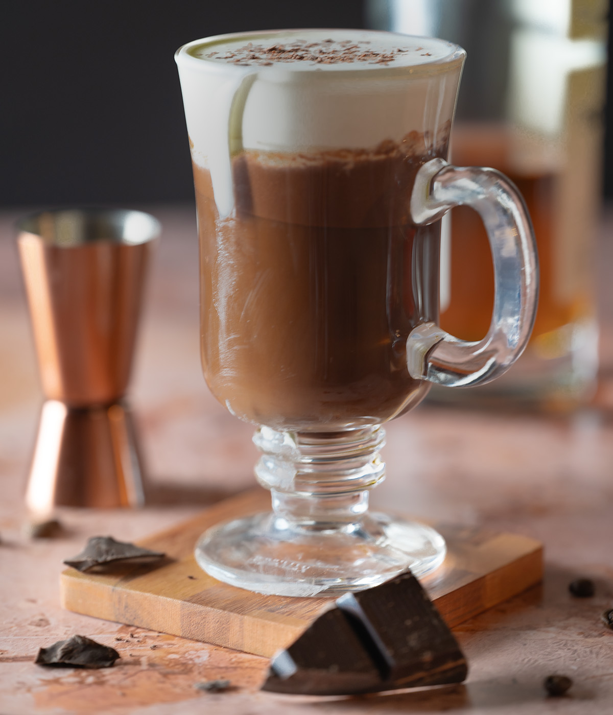 Chocolate Irish coffee with a bottle of whisky, a jigger, and piece of dark chocolate.