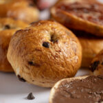 A chocolate chip bagel with hazelnut spread and strawberry jam.