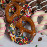 A half-dipped chocolate-covered pretzel with rainbow sprinkles.