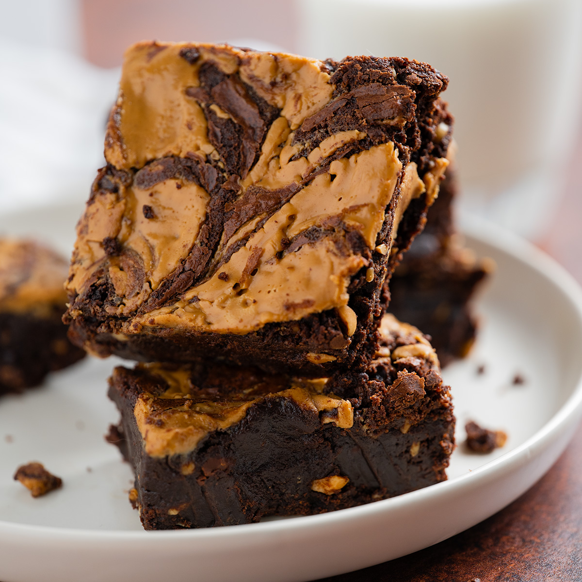 A tower of peanut butter brownies on a plate with a glass of milk.