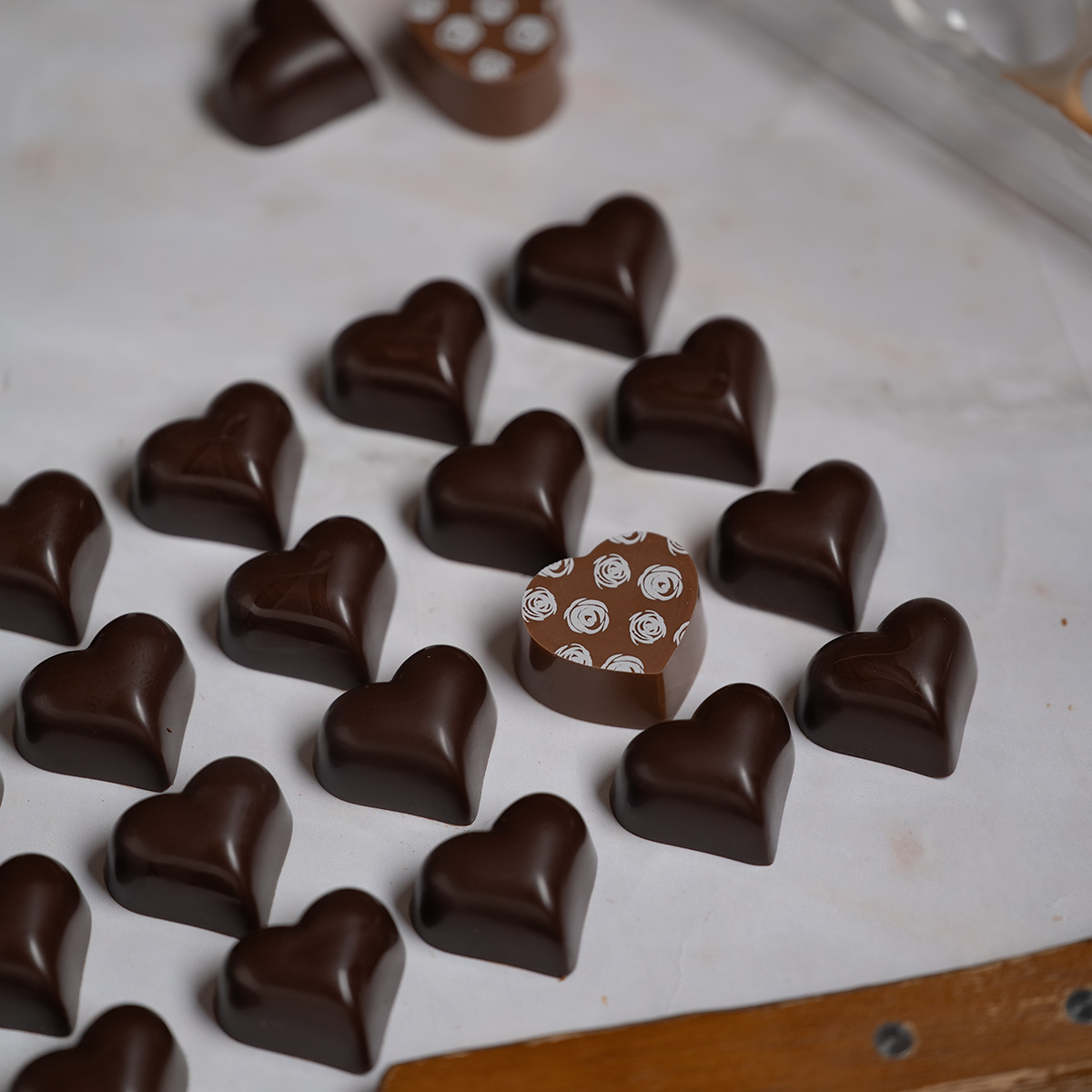 Rows of solid dark chocolate hearts with one milk chocolate heart.