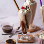 Three thick chocolate milkshakes served with various toppings.