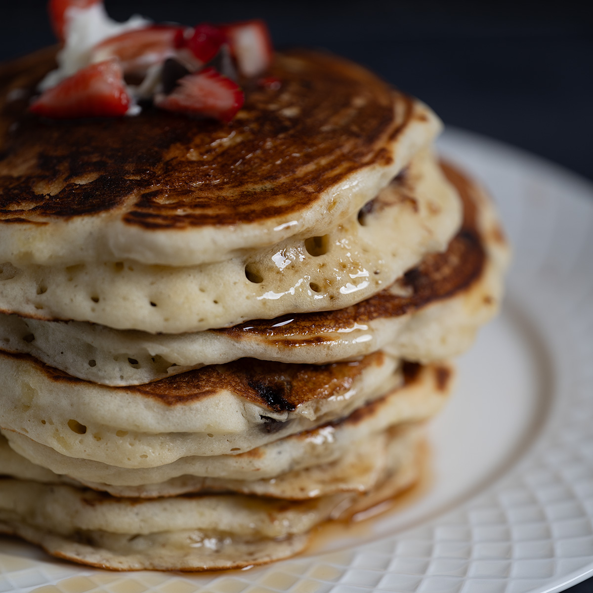 Tall, fluffy chocolate chip pancakes with maple syrup.