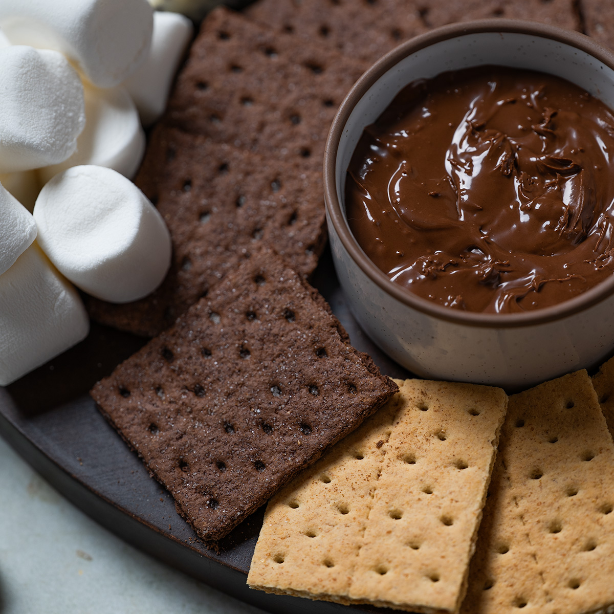 Chocolate spread and graham crackers and marshmallows on a s'mores charcuterie board.