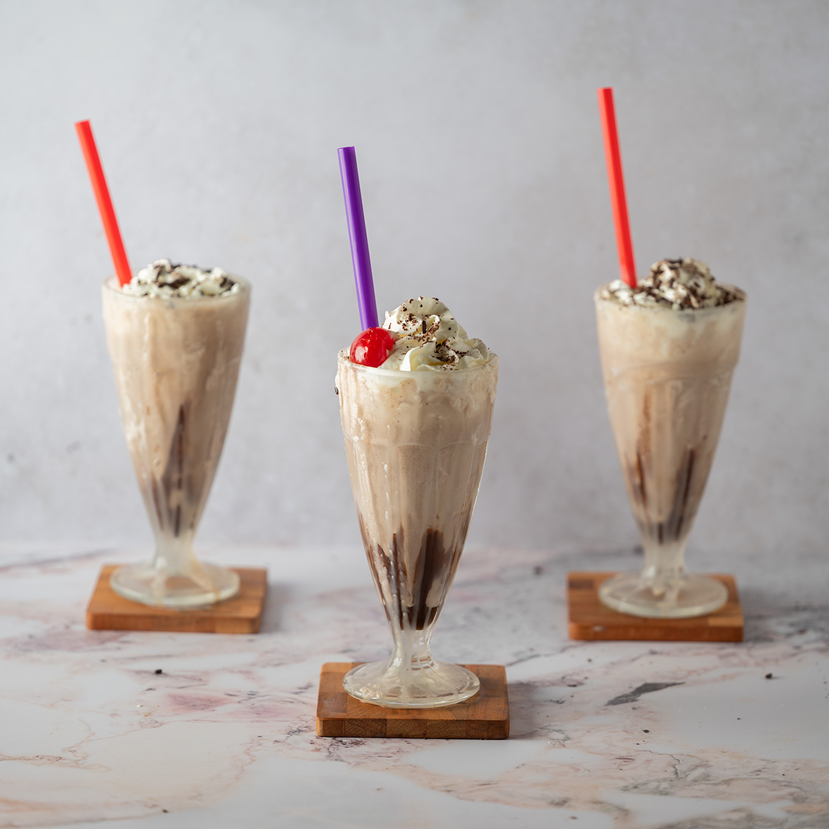 Three thick chocolate milkshakes staggered on a pink and grey background.