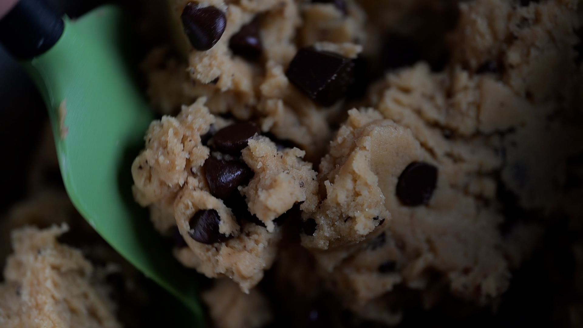 Video still showing the same rubber spatula folding chocolate chips into cookie dough